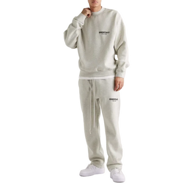 Person wearing a light gray sweatshirt and pants set with 'Essential' branding on a white background